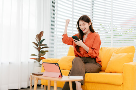 Beautiful Asian woman playing social media using smartphone at home. Woman is shopping and chatting with friends online.