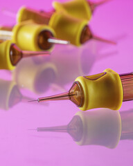 A close-up view captures a syringe with a vivid yellow casing, placed on a reflective pink surface....