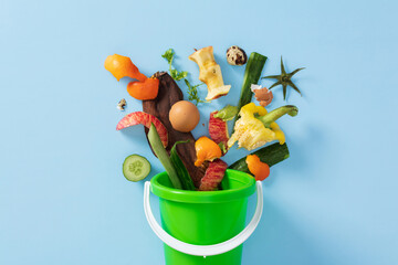 Organic food waste for composting in green bin on blue background.