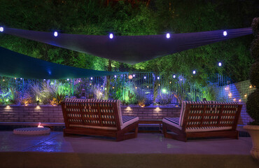 Rear view of teak lounge chairs in a desert oasis yard at night, overlooking a mountain lit by...