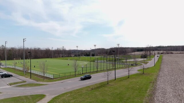 Aerial panning view of a car entering the parking lot beside a soccer field in Orillia, Ontario