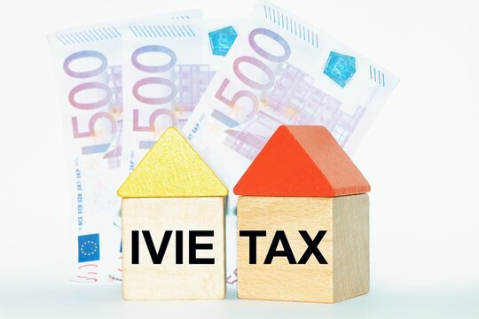 Wooden toy houses with 500 euros banknotes as background. Tax "Ivie"