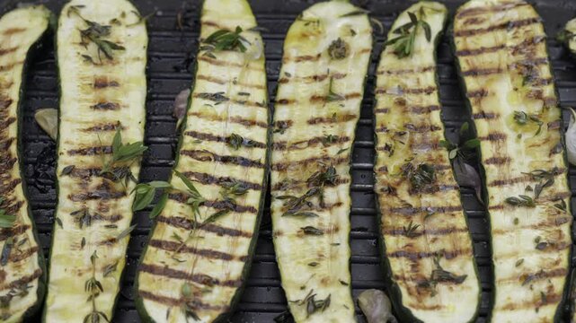  Grilled zucchini halfs with herbs and olive oil on a grill plate, top view