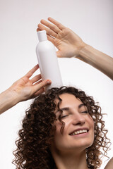 Portrait of an attractive cheerful long-haired curly-haired girl holding a bottle of soap, shampoo,...