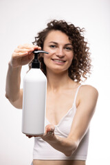 Portrait of an attractive cheerful long-haired curly-haired girl holding a bottle of soap, shampoo,...