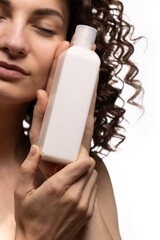 Portrait of an attractive cheerful long-haired curly-haired girl holding a bottle of soap, shampoo,...