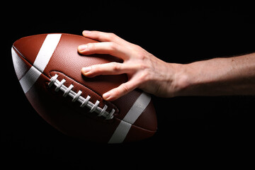 Close-up of an athlete's hand playing American football, holding a football in the air on a black background