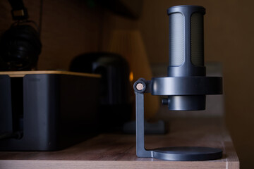 Close-up of a modern condenser microphone on a sleek desk with studio headphones and warm wood accents in a recording studio interior. Photo. High resolution
