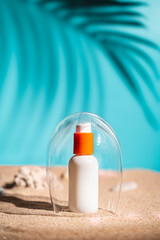 Sunblock or sunscreen in cosmetic tube under a glass dome as a symbol of sun protection on beach sand background. Summer vacation and skin care concept, spf uv-protect cosmetics. Skin health.