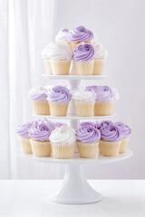 Cupcakes with purple and white frosting are arranged on a three-tiered stand. Dessert display, elegant cupcakes, sweet treat