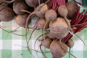 A neat row of earthy red beets, roots and greens attached, arranged on a market table