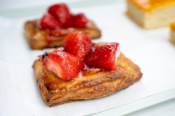 A flaky pastry topped with fresh strawberries, presented on a white surface