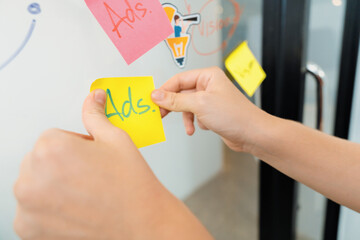 Closeup of professional businesswoman hand put and stick the colorful sticky notes on whiteboard...
