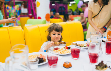 Cute little ukrainian girl having breakfast in restaurant and eating shish kebab. Preschooler...
