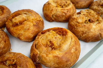 Golden-brown onion swirl pastries arranged neatly on a tray in a bakery setting.