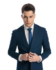 elegant young businessman buttoning navy blue suit and looking forward