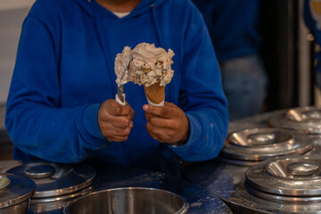 A server in a vibrant blue hoodie elegantly scoops generous portions of ice cream into a crisp...