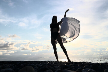 black silhouette of ona alone female lady Woman with White transparent Shirt Standing on a Pebble...