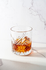 Whiskey with ice cube in the glass at white table.