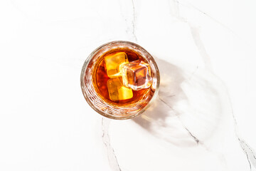 Whiskey with ice cube in the glass at white table.