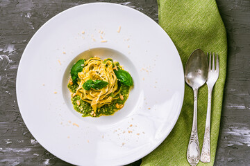 Italian cuisine. Fituccini al pesto on a white plate with a green napkin and cutlery with basil,...