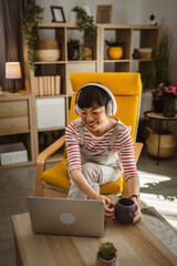 Japanese woman work on laptop computer at home wear headphones watch movie online or browse internet