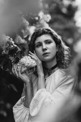 Young pretty caucasian woman in romantic outfit walking in blooming spring garden. Artistic outdoor photo of beautiful red-haired girl posing in fragrant lilac blossom.