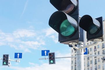 Traffic lights with green signal in urban street. Cloudy blue sky and buildings in background. Road...
