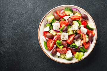 Greek salad in craft plate on black kitchen table. Top view. Vegan food.