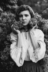 Young pretty caucasian woman in romantic outfit walking in blooming spring garden. Artistic outdoor photo of beautiful red-haired girl posing in fragrant lilac blossom.