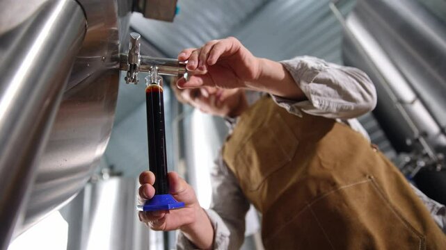 Brewer testing dark fresh beer for quality in stainless steel tank process at modern brewery