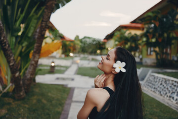Exotic woman standing in front of a palm tree with flower in hair on tropical island vacation
