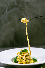Fituccini al pesto on a white plate and a fork with spaghetti wound on a gray background. Vertical...