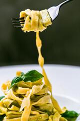 Fituccini al pesto on a white plate and a fork with spaghetti wound on a gray background. Vertical...