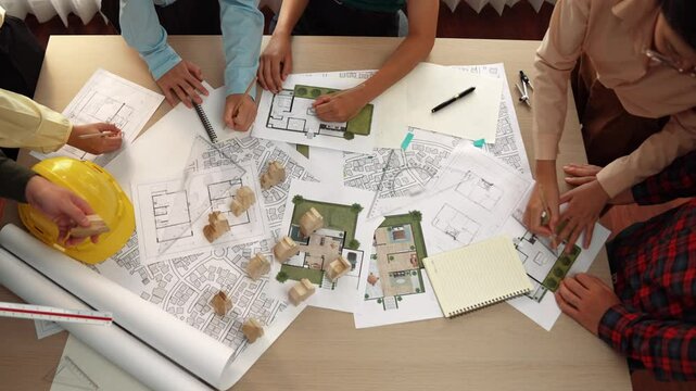Architect and safety engineer discussion about building construction use blueprint on table with architectural document, measurement tool and wooden block scatter around at modern office. Delineation.