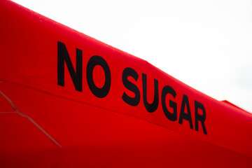 Horizontal street photo. Black inscription No sugar on red canopy of cafe. Slogan. Concept of suggesting dieting and eat less sugar for health, diabetes, food, pastry shop, confectionery, sweet store