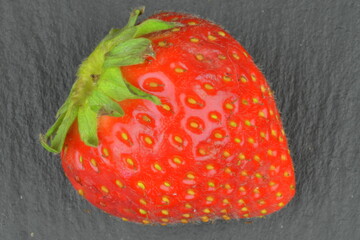 Macro shot of a ripe red strawberry on a black background. Ripe strawberry on a black slate backdrop. Close-up and top view