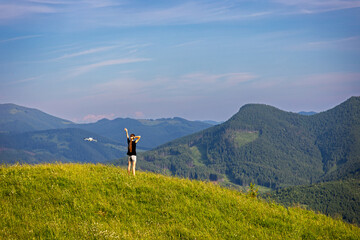 Drone Filming Girl on Scenic Mountain Hill. Young woman standing on a grassy hilltop posing for a...