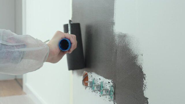 Detailed view of person using roller to paint wall black near electrical sockets during home renovation