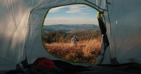A male traveler runs into his tent set on a scenic mountain slope. Filmed from inside the tent, the...