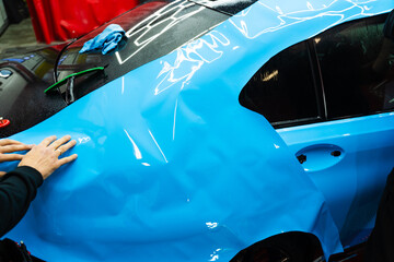 Applying PPF wrap on car during full detailing. Bold blue vinyl wrap installing in detailing...