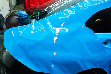 Applying PPF wrap on car during full detailing. Bold blue vinyl wrap installing in detailing...
