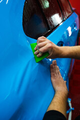 Applying a high-gloss blue PPF using a green squeegee ensures a bubble-free, smooth surface of car....