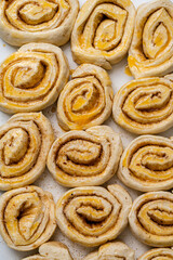 Making homemade cinnamon puff pastry buns. Raw dough rolls greased with egg yolk.