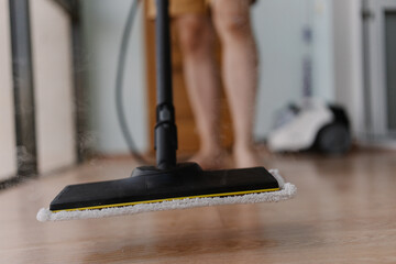 Wooden floor receiving deep cleaning through powerful steam mop, generating hot steamy vapor and...