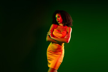 Confident young woman posing confidently in vibrant dress on dramatic green background