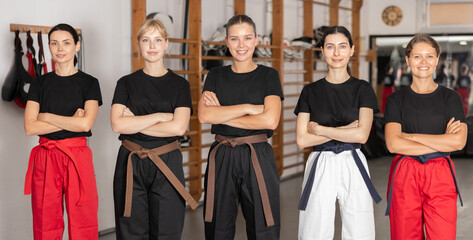Fototapeta premium Female team of young martial arts athletes in black uniform is standing in gym, public shoot, sports training camps. Preparation for competitions, sports as way of life..................