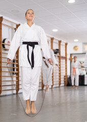 Young woman in kimono jumps rope in gym, performs warm-up. uses exercises to bring body into active...