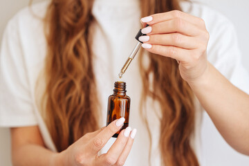 Woman using cosmetic dropper. Female hands with amber serum bottle. Closeup of skincare pipette application. Natural beauty product on white background. Healthy self-care and skin treatment concept.