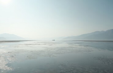 Obraz premium Scenic coastal landscape with tidal flats. Calm sea water, distant boat. Misty mountains, sky background, natural environment. Tranquil, serene, peaceful scenery. Ideal for travel eco projects.